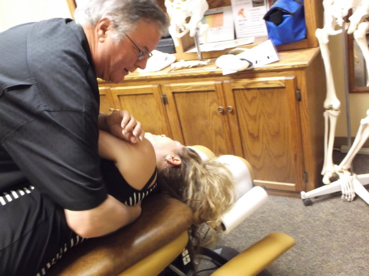 A chiropractor holds up a patient and helps her with her shoulder and back pain.
