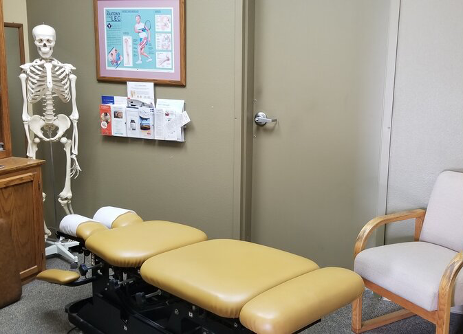 A chiropractic bed sits unattended at the Whalen Chiropractic office. There is a skeleton model in the corner.