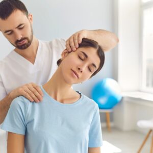 A chiropractor works with a client. He is wearing a white shirt and making an adjustment to her neck.