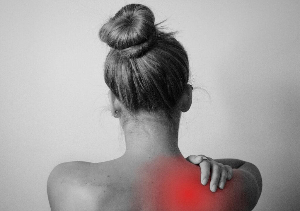 A woman holds her shoulder. She is experiencing shoulder pain.