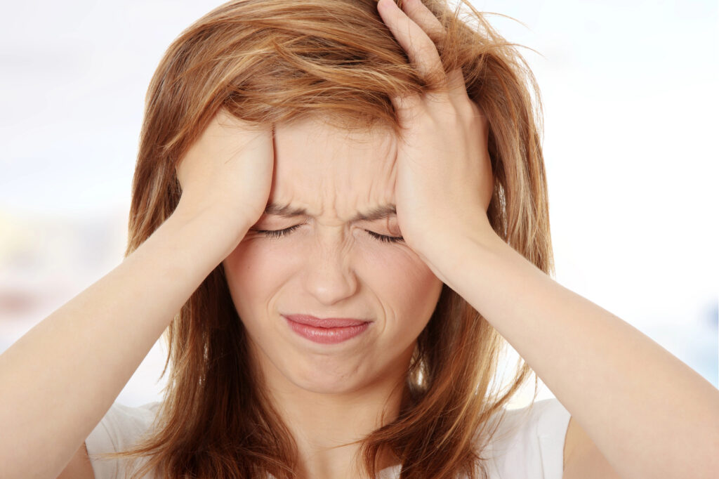 A woman is holding her head with both of her hands. She is experiencing a headache.