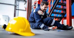 A worker sits on the ground. He is holding his shoulder and is feeling pain.